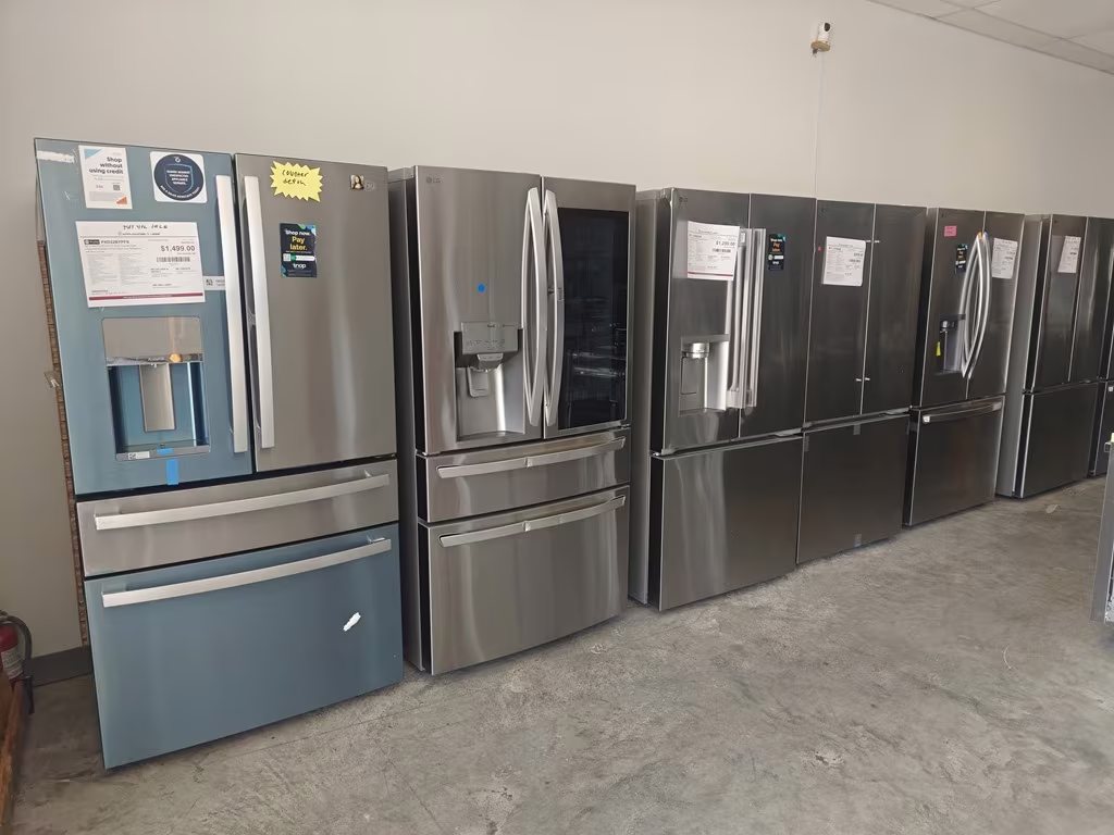 A row of French-door refrigerators with price sheets on the showroom floor
